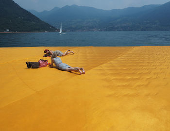 Man relaxing by sea against mountains