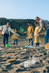 Grandparents and grandchildren cleaning while standing at beach