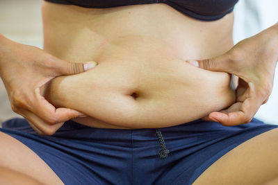 Midsection of woman holding belly at home 