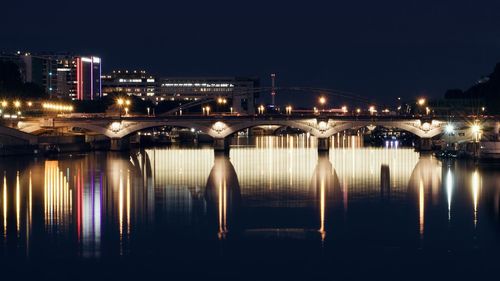 Illuminated bridge over river against sky at night