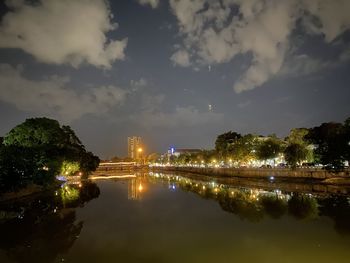 Illuminated buildings by river against sky at night