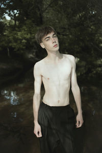 Portrait of shirtless man standing in forest