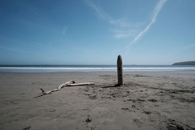 Wooden post in sand at beach against sky