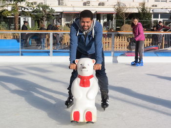 Smiling man ice-skating with polar bear toy on rink