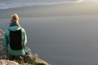 Rear view of woman sitting by sea against sky