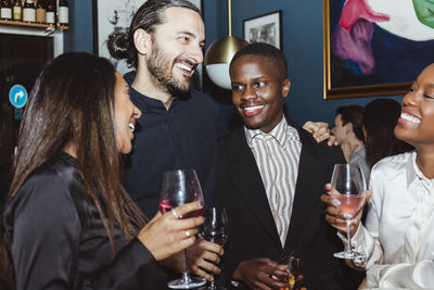 Happy male and female friends celebrating while having wine in restaurant