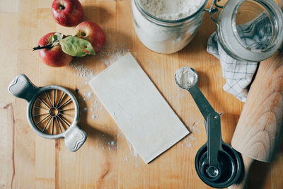 High angle view of apples with flour and kitchen utensils on wooden table