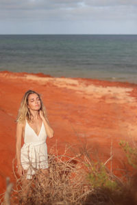 Beautiful young blonde woman in white dress on red sandy beach on the west coast of australia