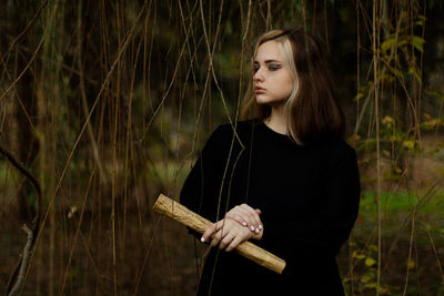 Young woman looking away while standing against plants