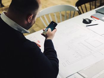 High angle view of architect using mobile phone while making blueprint in office