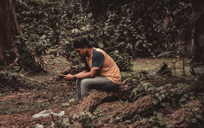 Side view of young man sitting in forest