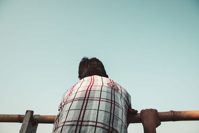 Rear view of man standing on railing against clear sky