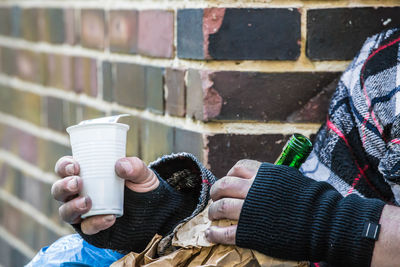 Midsection of man holding paper cup and bottle against brick wall