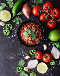 Bowl of fresh salsa with the ingredients and on black slate counter.