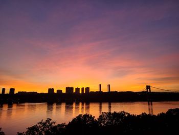 Silhouette buildings by lake against sky during sunset