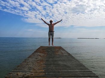 Shirtless man levitating over pier at beach against sky