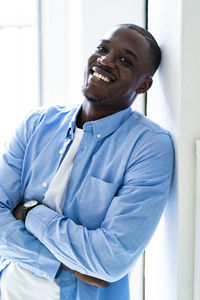 Happy man with arms crossed leaning on wall at home