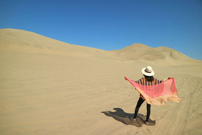 Rear view of woman with scarf standing at desert against clear sky