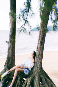 Woman on tree trunk by sea against sky