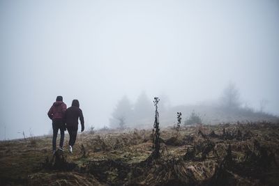 Rear view of man and woman walking on field in foggy weather