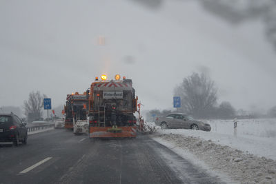 Vehicles on road against sky during winter