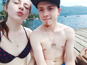 Portrait of young man with girlfriend sitting on jetty by lake