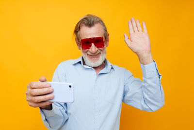 Smiling businessman gesturing during video call against yellow background