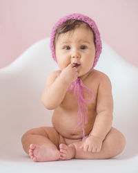 Close-up portrait of cute baby sitting against pink background