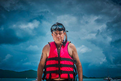 Portrait of man wearing life jacket against sky
