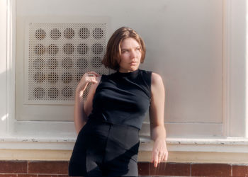 Portrait of young woman standing against wall