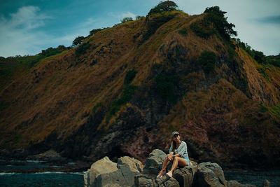 Woman sitting on rock against mountains