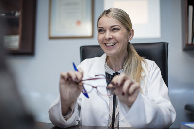 Female optometrist talking to patient, holding spectacles