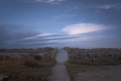 Footpath amidst field against sky