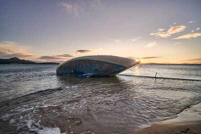 Boat moored on beach against sky during sunset