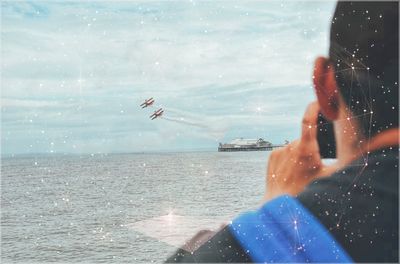 Rear view of man photographing airplanes flying over sea