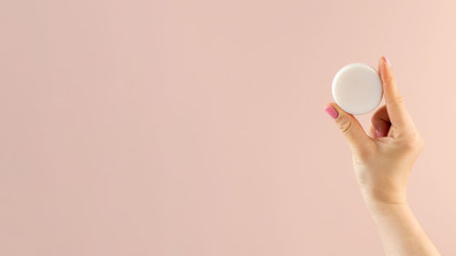 A woman's hand holds a round piece of soap on a light pink background. banner