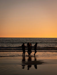 Silhouette people on beach against sky during sunset