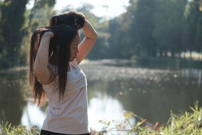 Young woman with hands in hair standing against lake