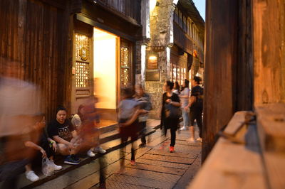 Blurred motion of people walking on footpath by buildings in city