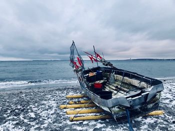 Boat moored at beach against cloudy sky