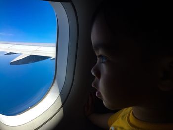 Close-up of boy looking through airplane window