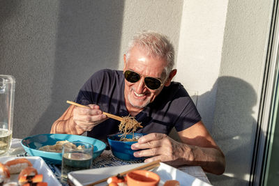 Attractive middle-aged man have fun while eating sitting on table laid chinese food in front of wall