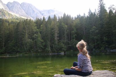 Full length of woman sitting by lake against mountains