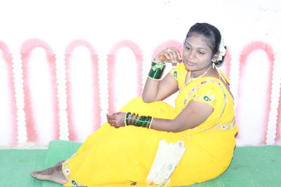 Portrait of a smiling young woman sitting against wall