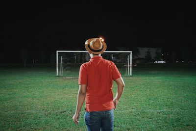 Rear view of man standing against goal post at night