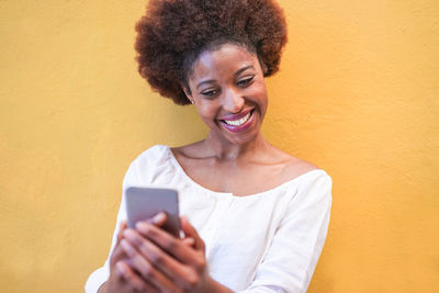 Smiling young man using mobile phone against wall