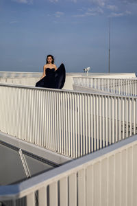 Woman sitting on railing against sky