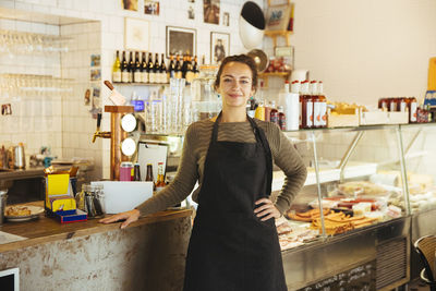 Portrait of confident young female owner standing with hand on hip at cafe