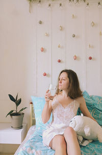 Beautiful woman holding water glass sitting on bed