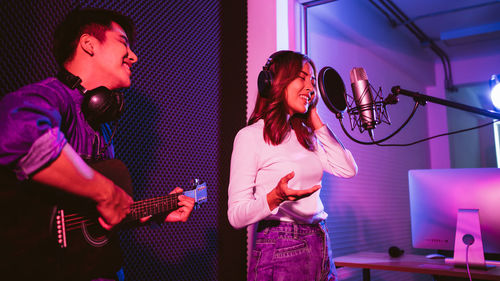 Woman singing song while man playing guitar at recording studio